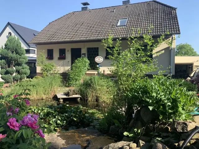 Außenansicht des Hauses Am Vogelherd 3 mit Gartenteich und blühenden Pfingstrosen