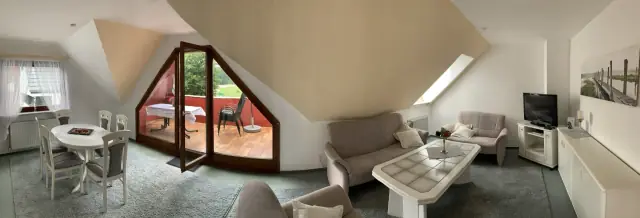 Wohnzimmer der Ferienwohnung mit Sitzgruppe, Essplatz und offener Balkontür